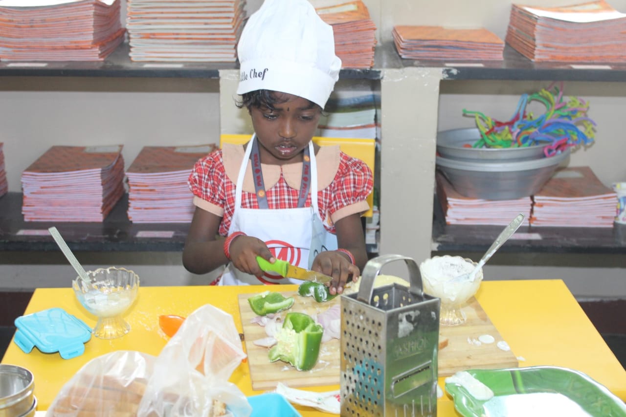 Child, dressed as a “little Chef” is cutting vegetables in a cooking activity, “fireless fusion”. (1)