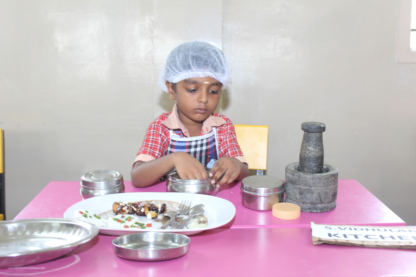 Child dressed as a “little Chef” is cutting vegetables in a cooking activity, “fireless fusion”.